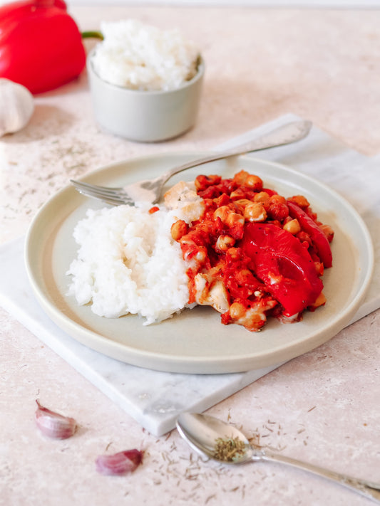 Portion von vegane Paprika-Feta-Kichererbsen-Pfanne neben einer Schüssel mit weißem Reis, garniert mit einem gegrillten roten Paprika, präsentiert auf einem hellen Teller