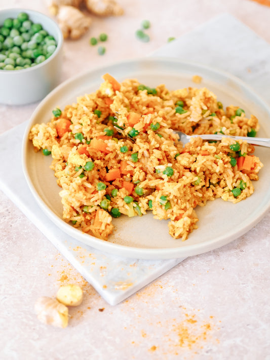 Veganer Eier-Reis serviert auf einem hellen Keramikteller, bestreut mit frischen Erbsen und Karottenstücken, neben einer Schale mit grünen Erbsen
