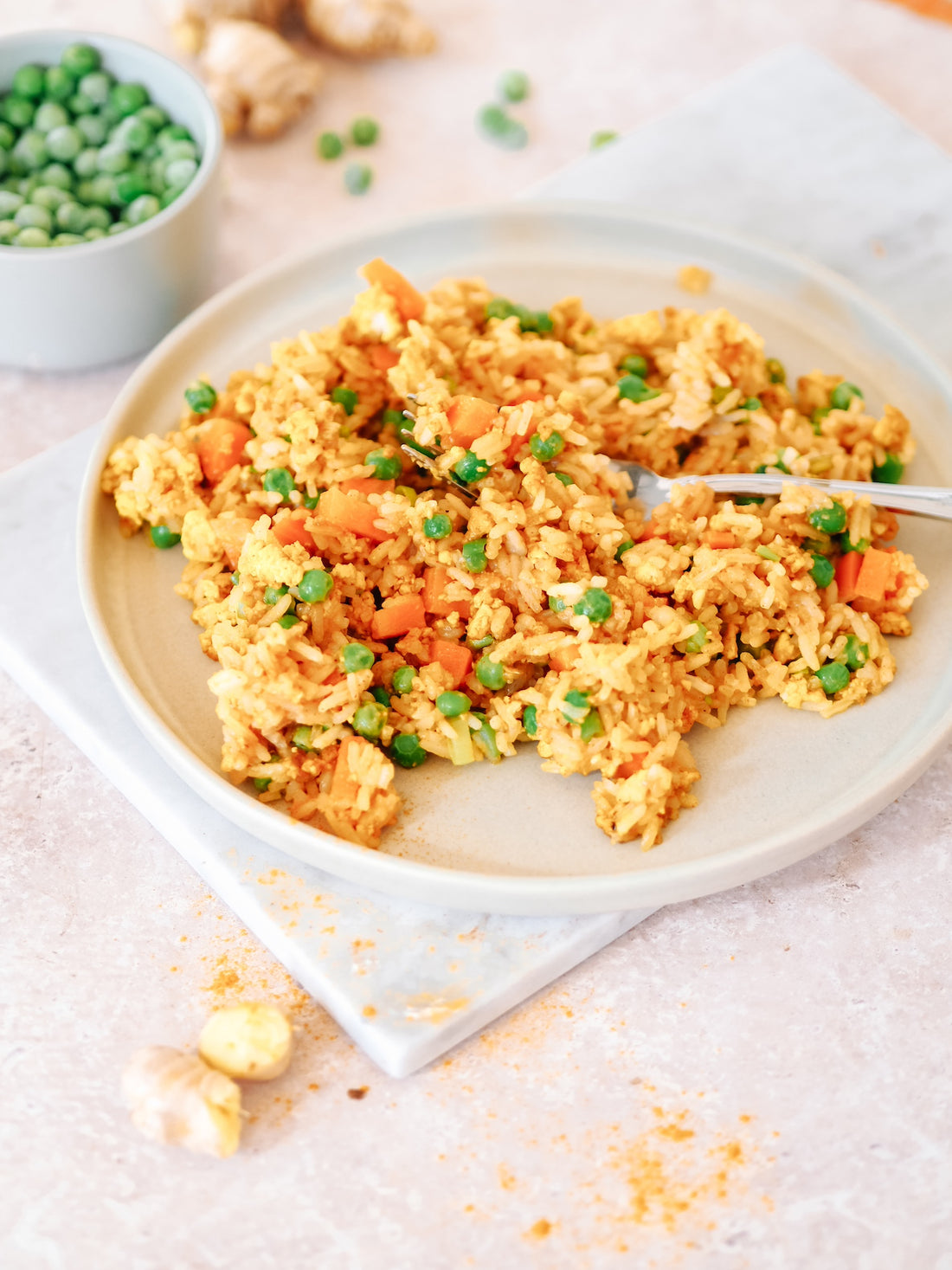 Veganer Eier-Reis serviert auf einem hellen Keramikteller, bestreut mit frischen Erbsen und Karottenstücken, neben einer Schale mit grünen Erbsen
